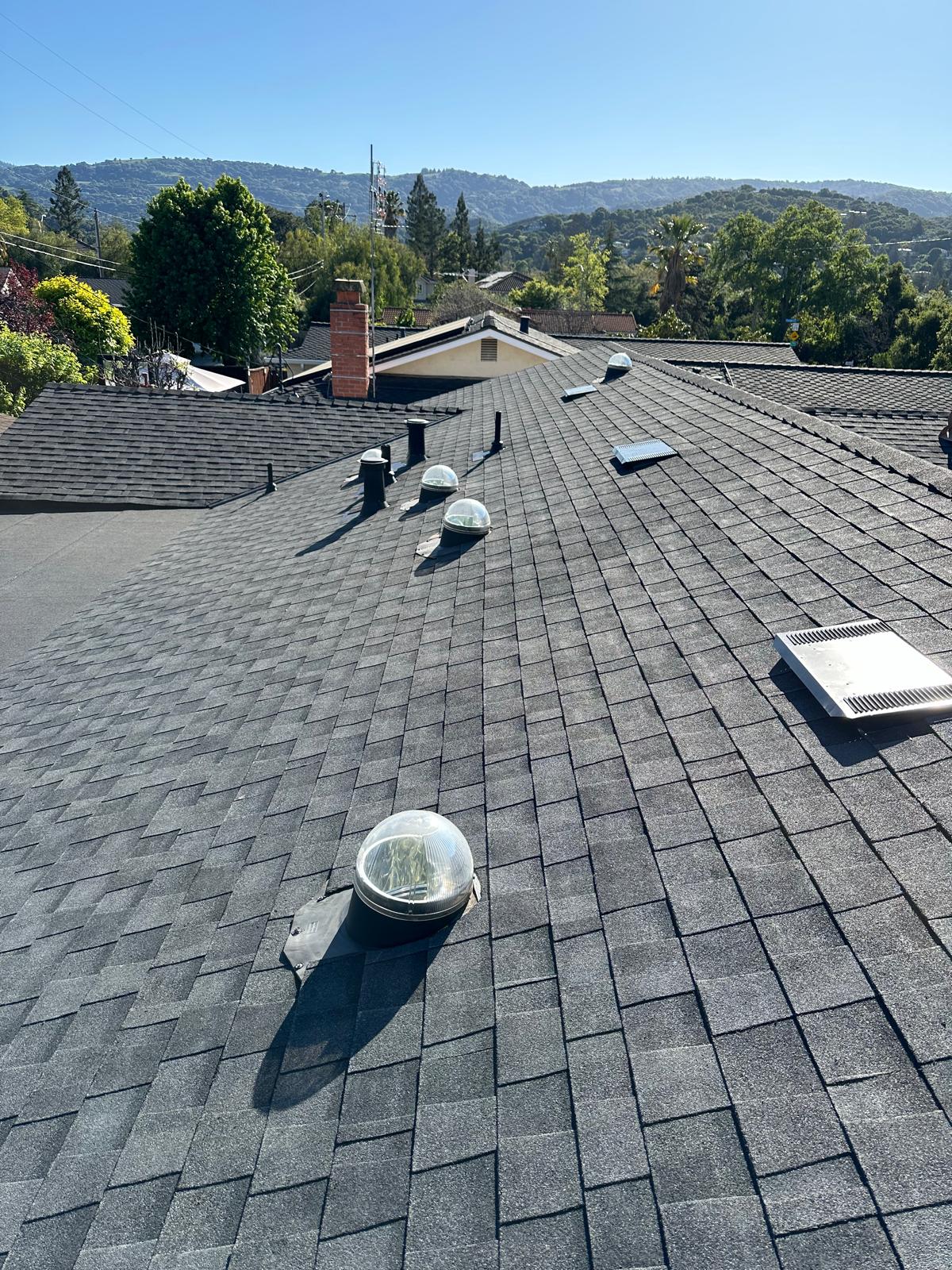 Gray shingle roof with dome skylights and metal attic vents, hills in the distance