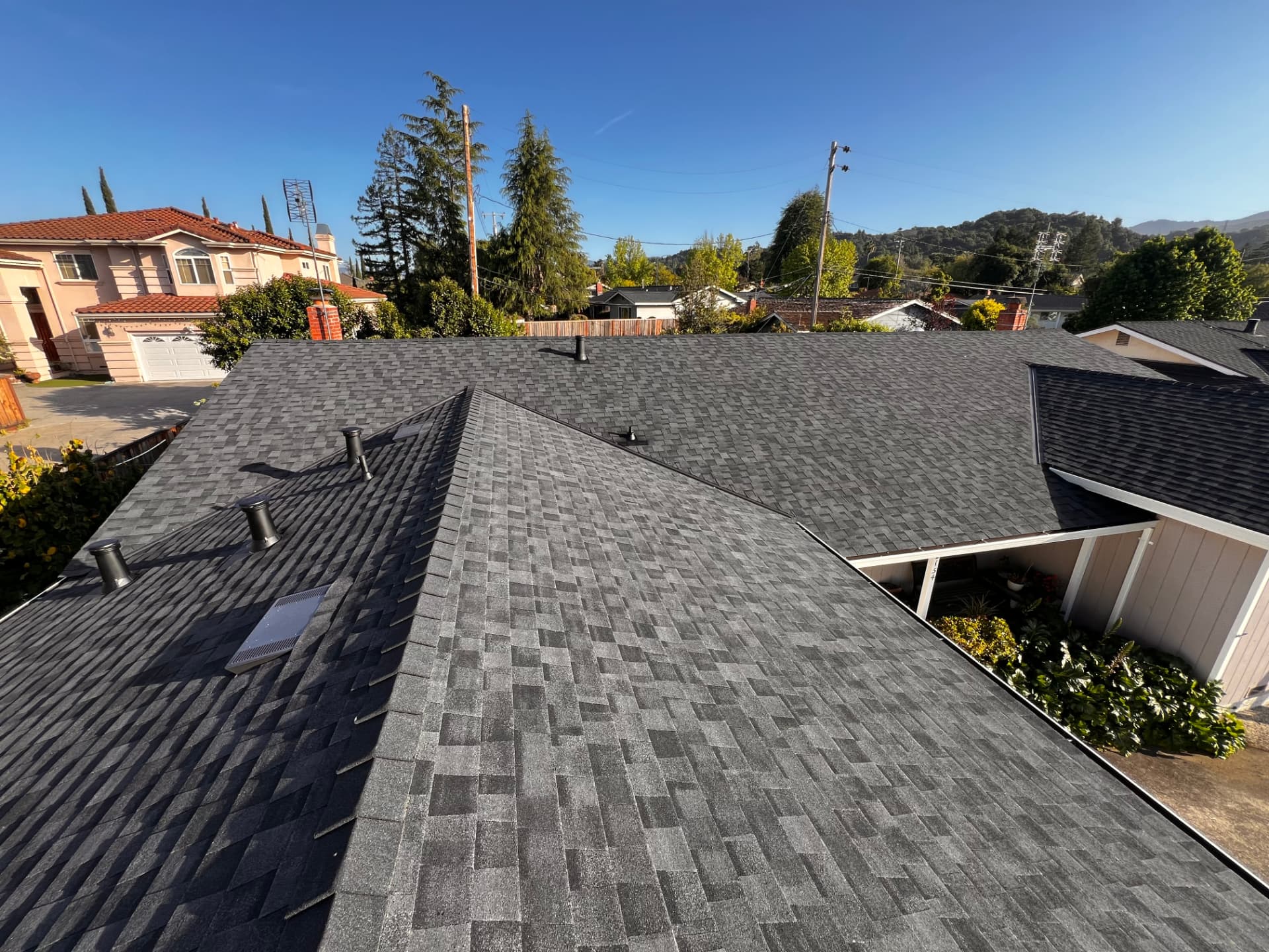 Gray shingle roof with black vent pipes and an attic vent overlooking a residential street