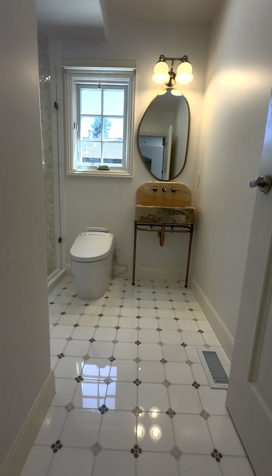 Powder room with stone console sink, brass-framed oval mirror and patterned tile floor