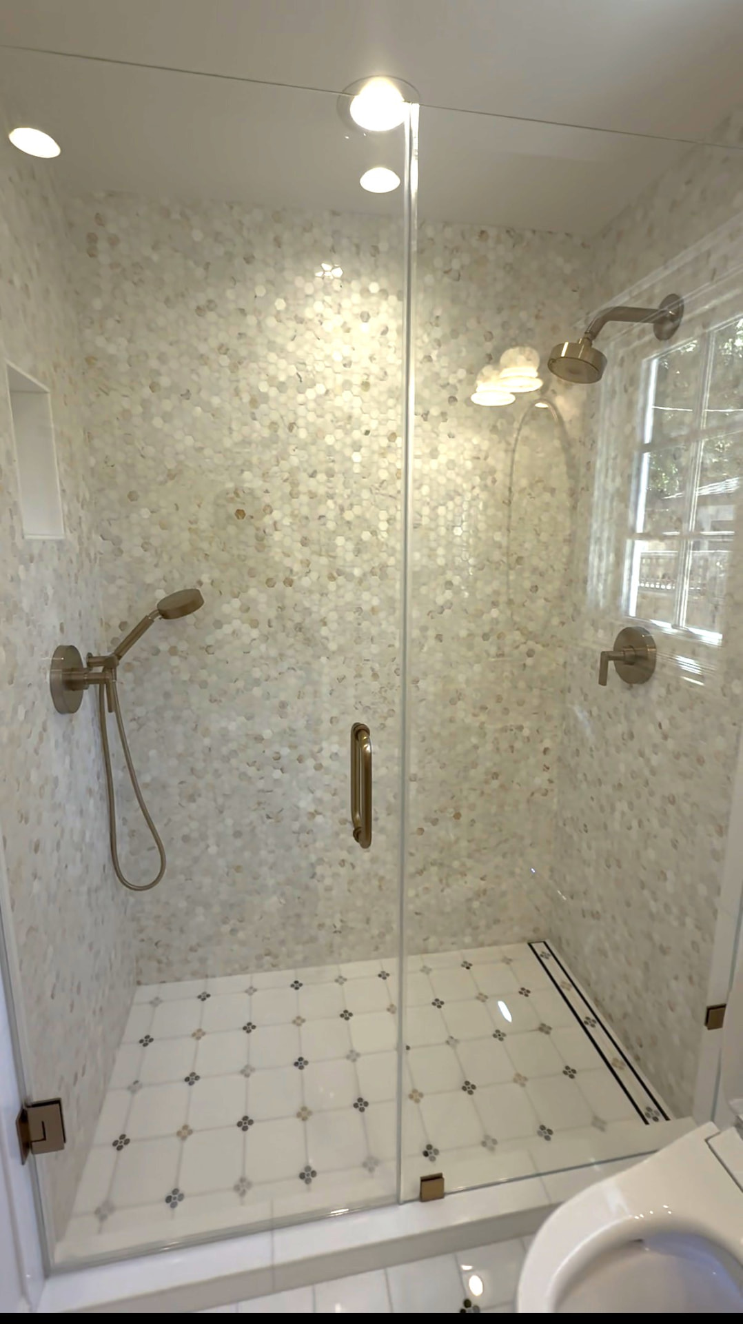 Walk-in shower with marble mosaic tile walls, glass door and patterned floor tile