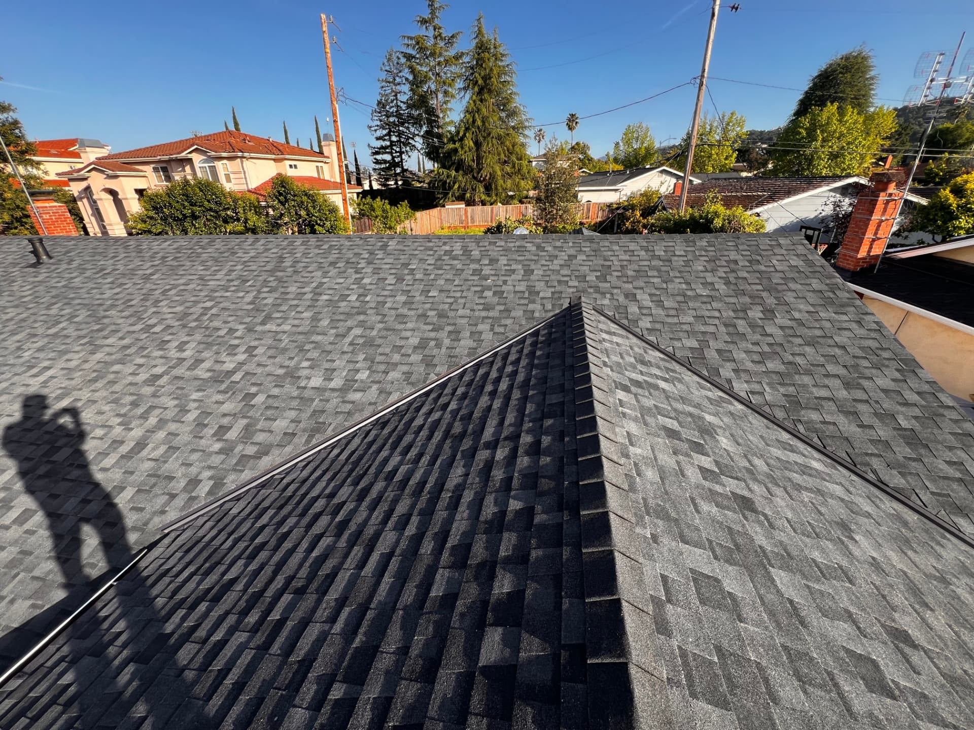 Gray shingle roof ridges meeting at a peak with a brick chimney nearby