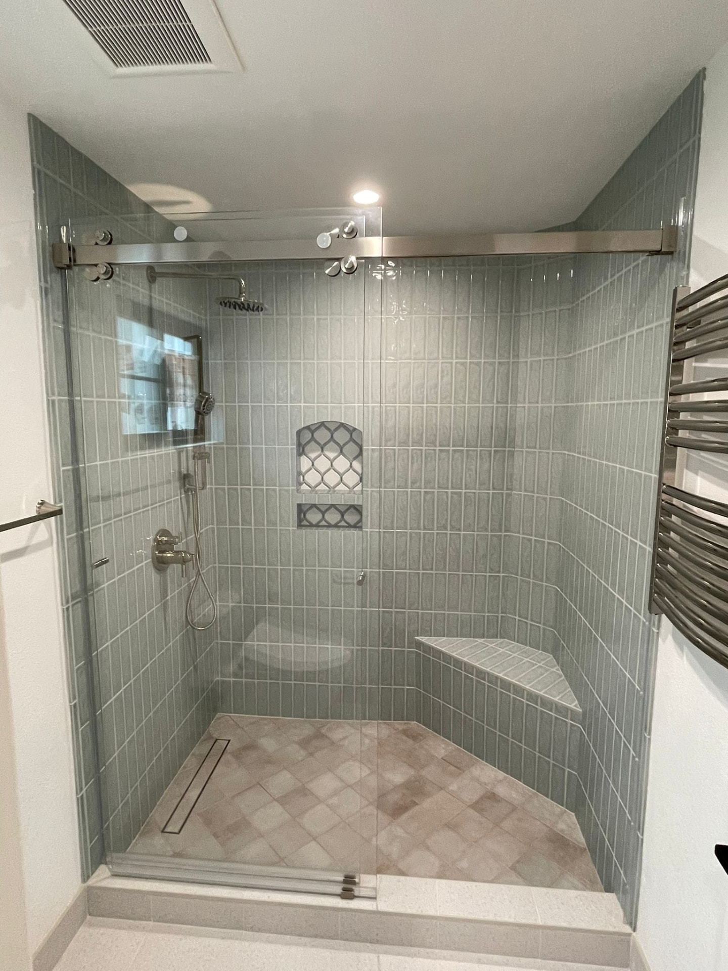 Walk-in shower with light green vertical stacked tile, glass sliding door, built-in niche and corner bench