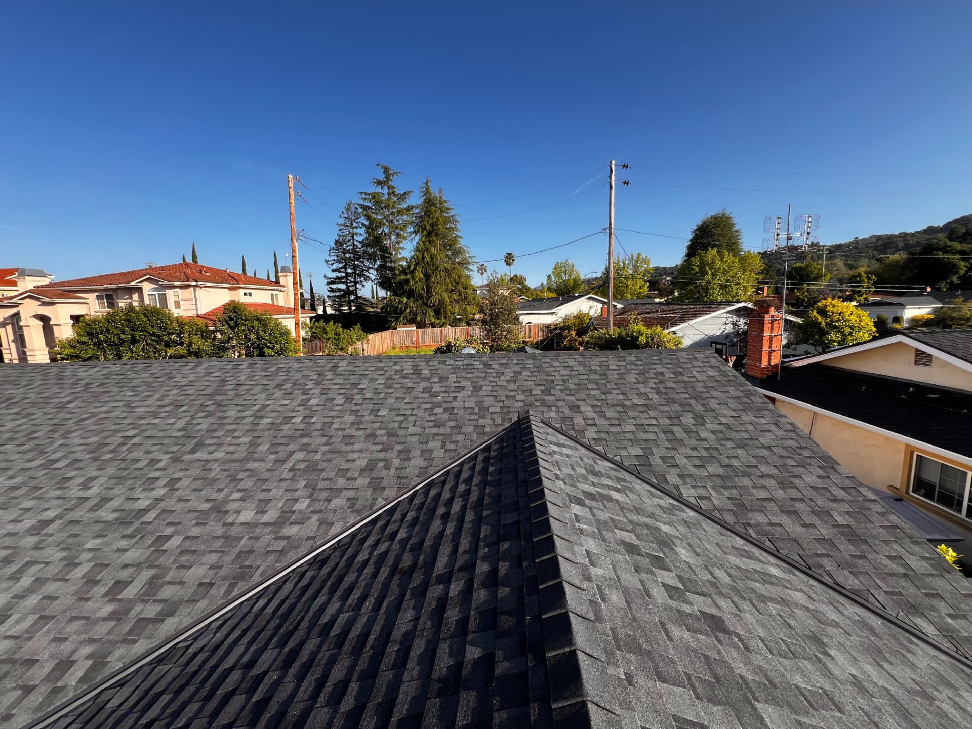 Gray shingle roof with a long ridge line, viewed across neighboring rooftops and trees
