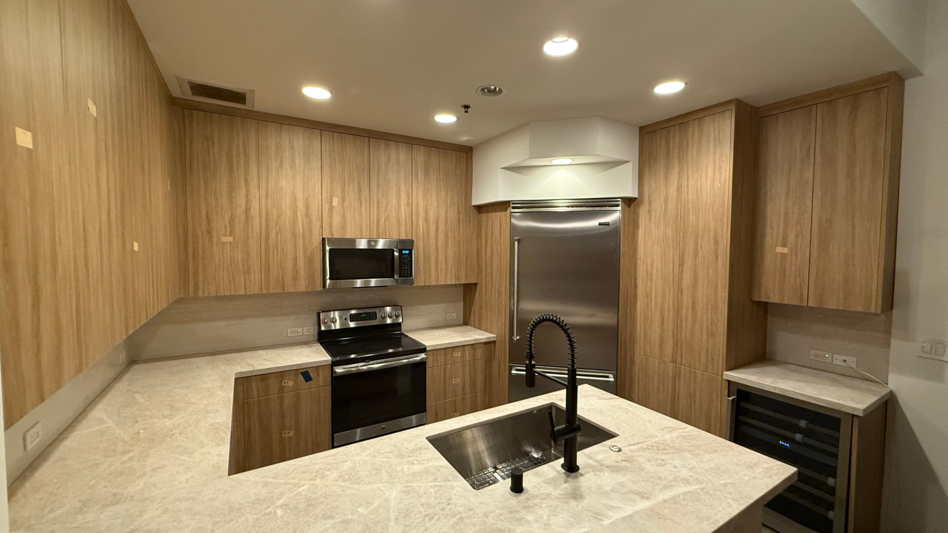 Modern kitchen with light wood-look cabinets, marble countertops, stainless steel appliances, and a large center island