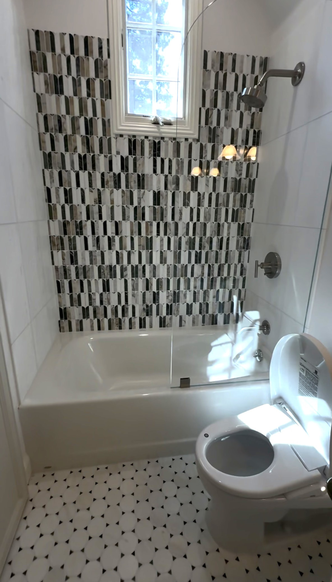 Bathtub with glass shower panel and marble mosaic tile surround