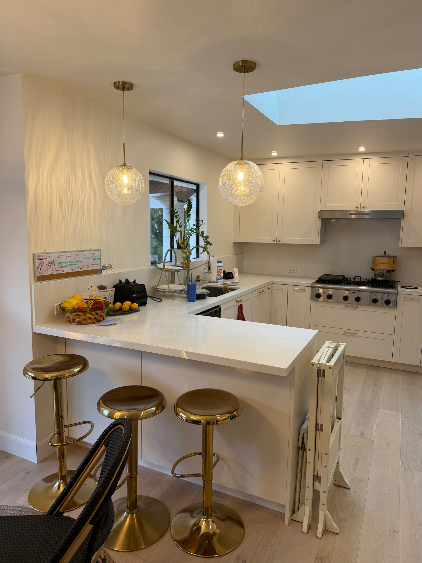 Finished kitchen with white cabinets, brass pendant lights, marble countertops, brass bar stools, and a skylight